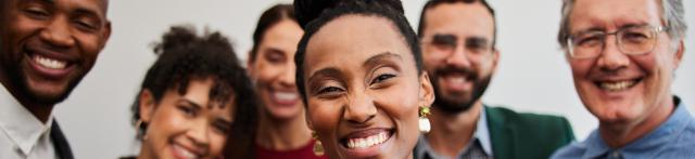 A group of smiling individuals poses together, all looking directly at the camera with cheerful expressions.