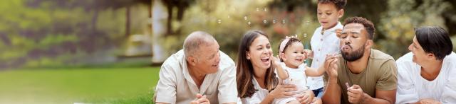 A smiling family sits together on the grass, enjoying a sunny day outdoors. 